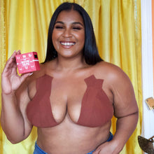 Load image into Gallery viewer, A woman with a darker skin tone using The Boob Tape in brown color and holding the box of The Boob Tape product.